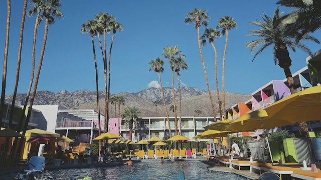 Swimming pool, yellow umbrellas, and colorful hotel balconies beneath palm trees at The Saguaro in Palm Springs.