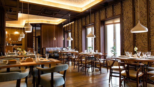 Restaurant dining room with wooden tables, upholstered chairs, and warm pendant lighting.
