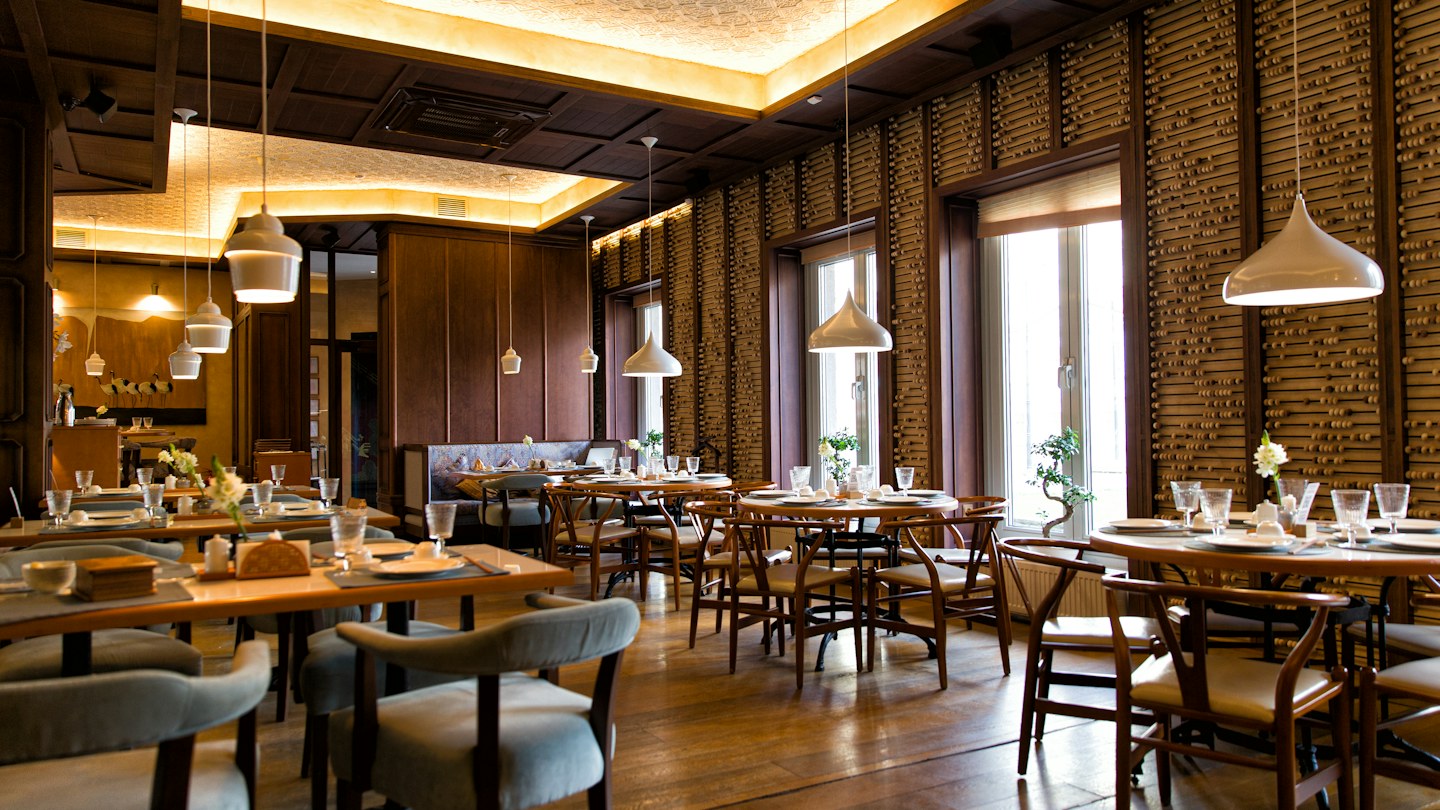 Restaurant dining room with wooden tables, upholstered chairs, and warm pendant lighting.