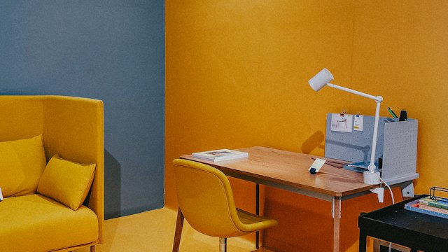 Creative workspace with a yellow chair, mustard wall, wooden desk, and white task lamp.