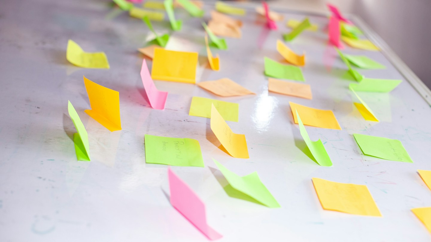 Pink, yellow, green, and peach sticky notes arranged across a white surface for brainstorming and planning.